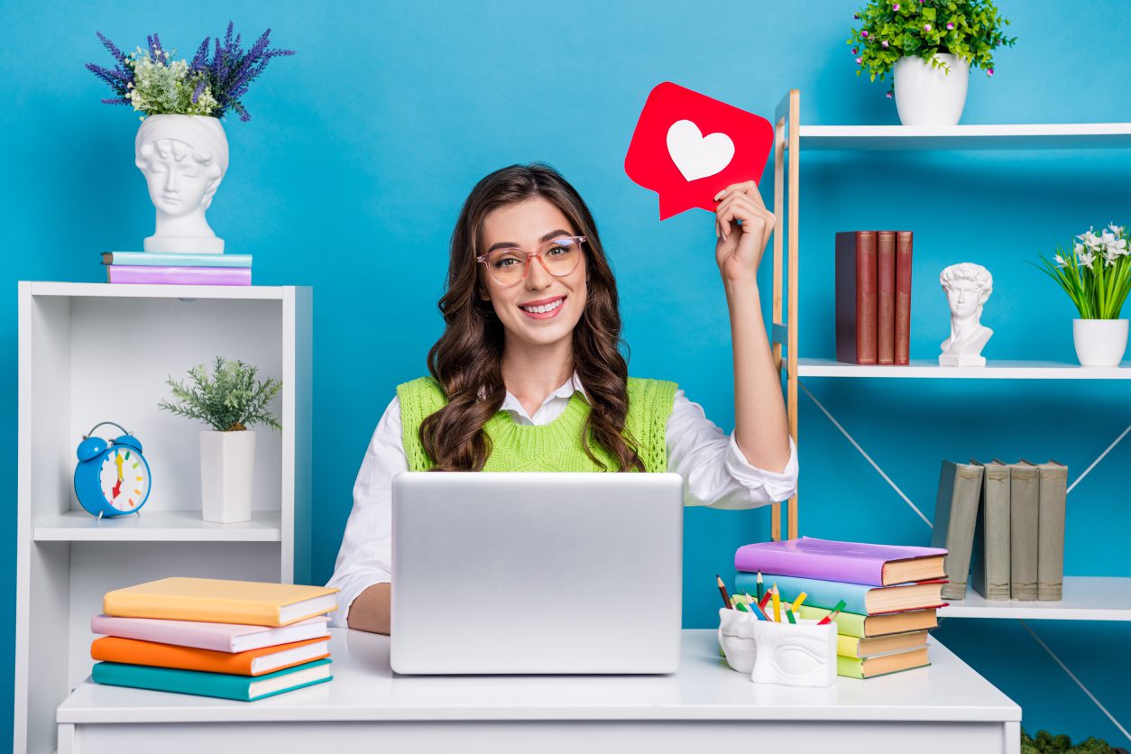 Smiling woman holding heart icon at desk.