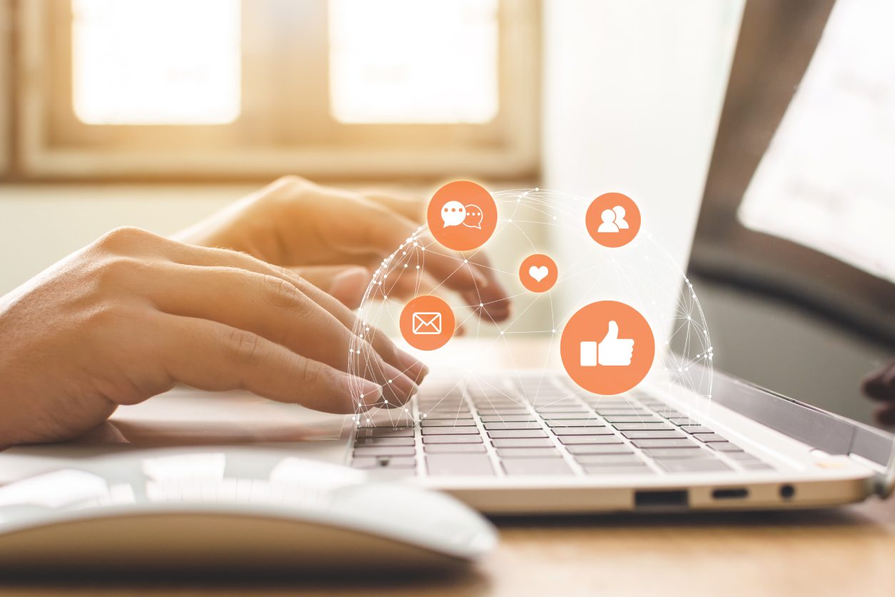 Hands typing on laptop with social icons.
